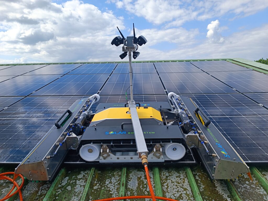 Robot nettoyeur de panneaux solaires en action sur le toit d’un bâtiment industriel sous un ciel partiellement nuageux."